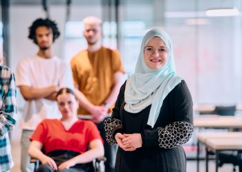 A diverse group of young business people walking a corridor in the glass-enclosed office of a modern
