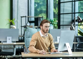 Serious and scorn-centered man in the office at work with a computer, man typing thoughtfully on