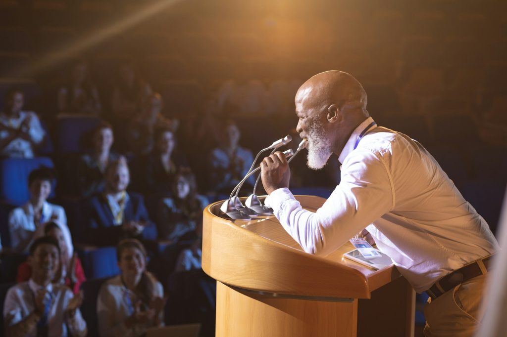 Old businessman standing and holding speaker to speak in the auditorium