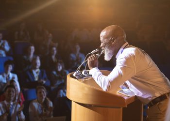 Old businessman standing and holding speaker to speak in the auditorium
