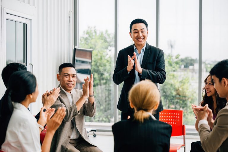 A seminar leader imparts wisdom to a diverse audience, and participants actively raise their hands