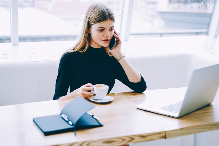 Administrative assistant having hot drink and talking on mobile phone