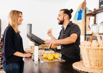 Customer Engaging in Friendly Conversation With Smiling Storekeeper at Grocery Checkout