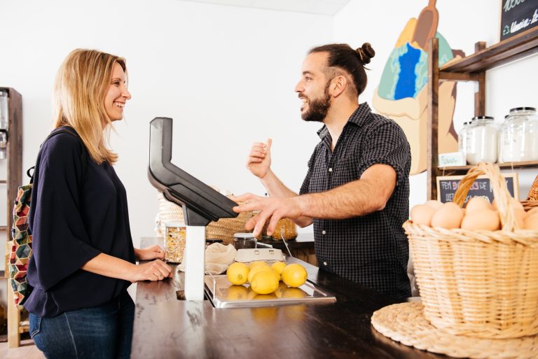 Customer Engaging in Friendly Conversation With Smiling Storekeeper at Grocery Checkout