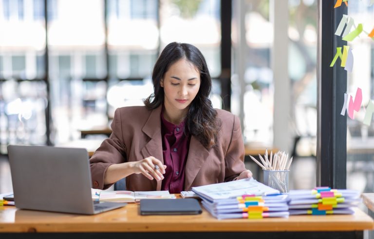 Freelancer Happy business Asian woman in knitwear taking notes at laptop sitting at desk office,