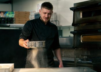 in a professional kitchen in a pizzeria young chef sifts flour on the table