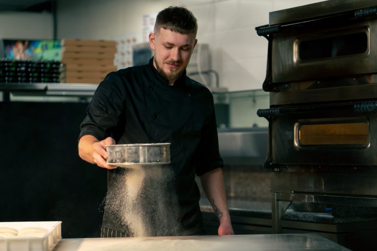 in a professional kitchen in a pizzeria young chef sifts flour on the table