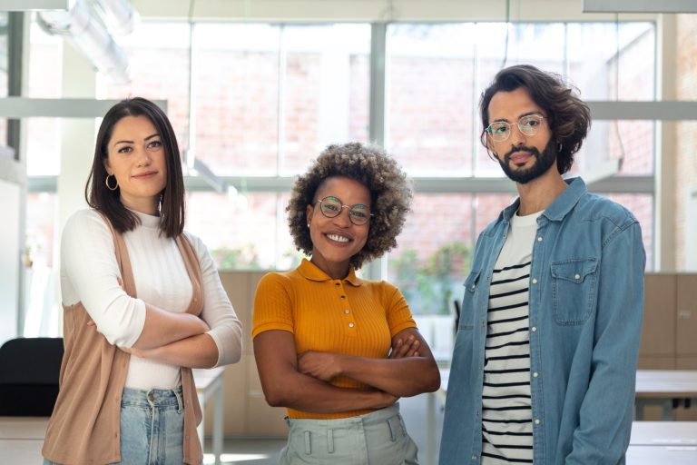 Multiracial coworkers looking at camera standing in bright spacious co working office space.