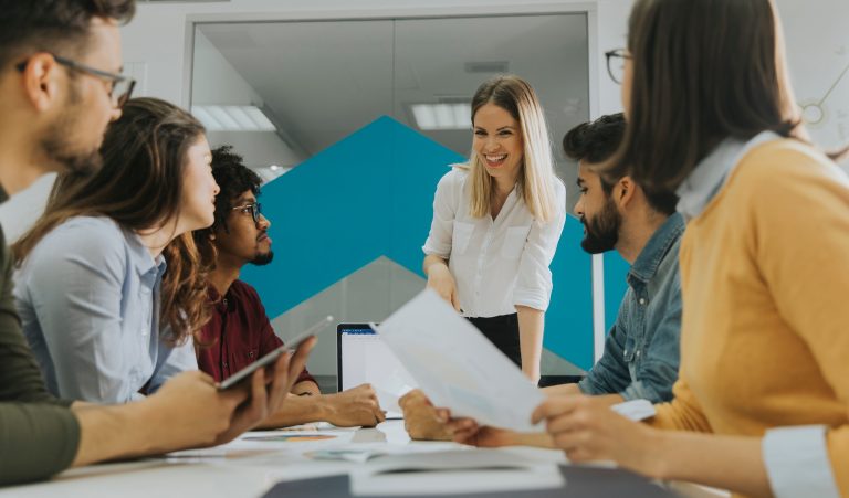 Pretty female team leader talking with mixed race group of people in the office