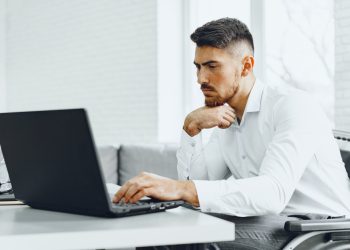 Serious concentrated man in wheelchair using his laptop for work / seeking a job in internet