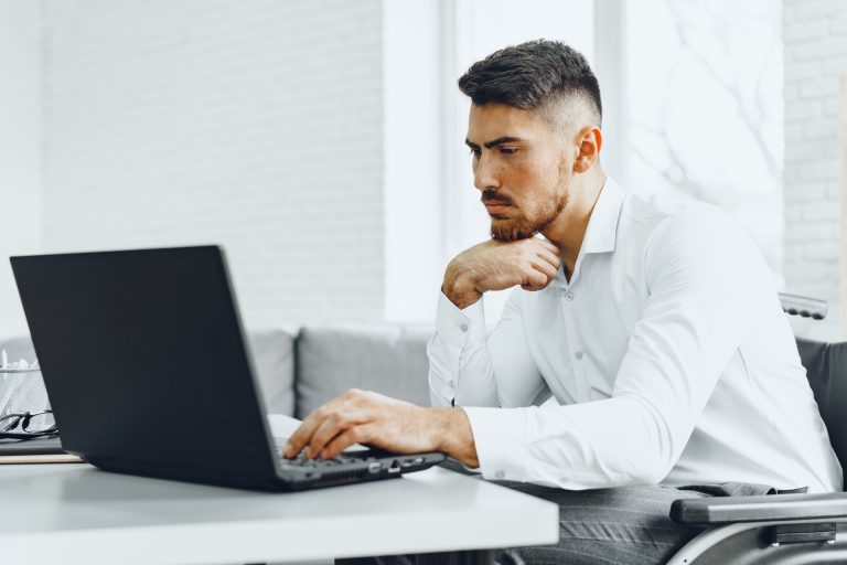 Serious concentrated man in wheelchair using his laptop for work / seeking a job in internet