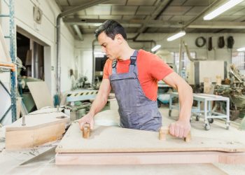 Skillful carpenter cutting wooden board with router