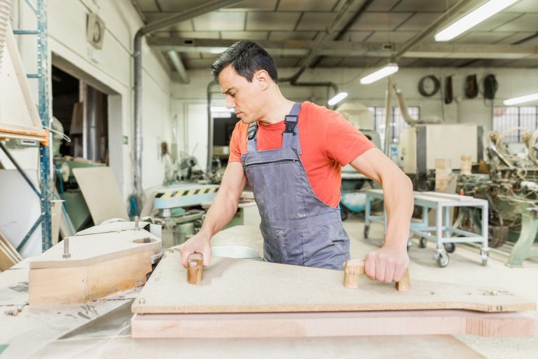 Skillful carpenter cutting wooden board with router