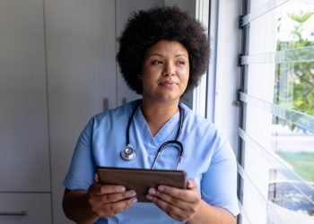 Smiling african american mid adult female nurse looking away while holding digital tablet