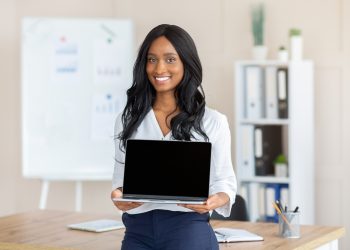 Smiling black female manager holding laptop with empty screen at workplace, mockup for your website