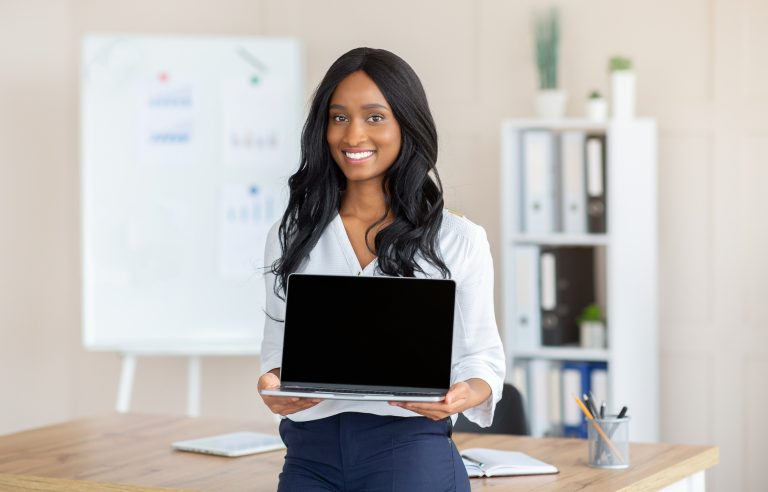 Smiling black female manager holding laptop with empty screen at workplace, mockup for your website