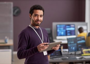 Smiling software engineer holding digital tablet while standing in tech office