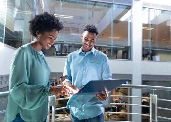 Smiling young african american professionals discussing together over file on staircase at workplace