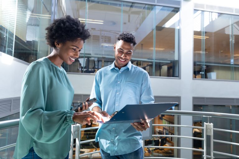 Smiling young african american professionals discussing together over file on staircase at workplace