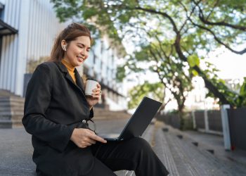 Smiling young Asian business woman using laptop sitting outdoor. hybrid working, searching job