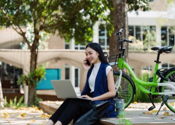 Young businesswoman sitting on stair in city park and using laptop for work hybrid. Bike to work eco