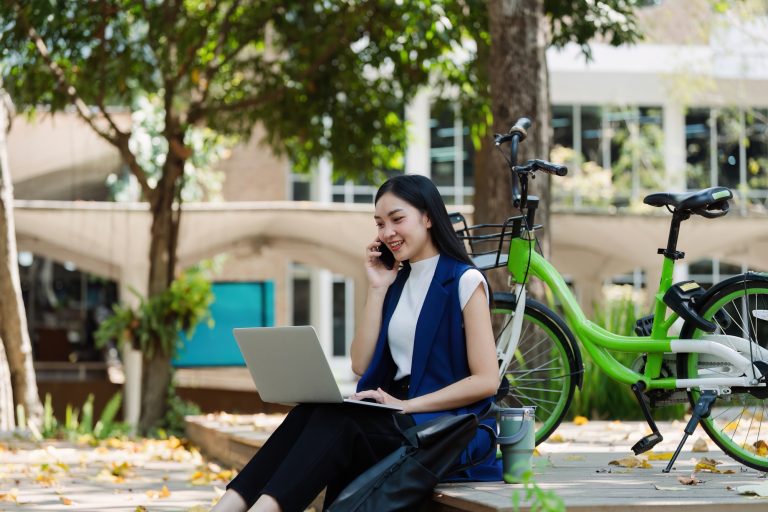 Young businesswoman sitting on stair in city park and using laptop for work hybrid. Bike to work eco