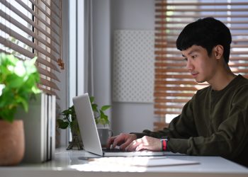Young man freelancer searching online information, working with laptop computer at home office.