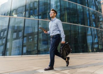 A businessman walking confidently with a briefcase and tablet, dressed in professional attire,
