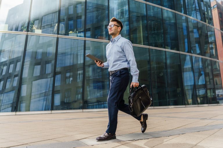 A businessman walking confidently with a briefcase and tablet, dressed in professional attire,