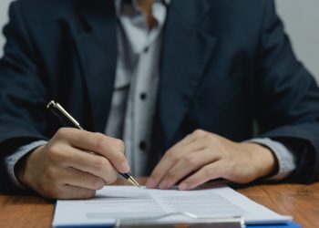 Businessman holding a pen signing a document, law ,job search, write a personal contract on desk.