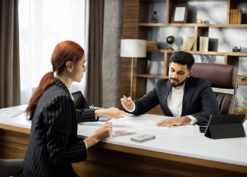 Confident businessman in black suit gives a salary to young red hair businesswoman.