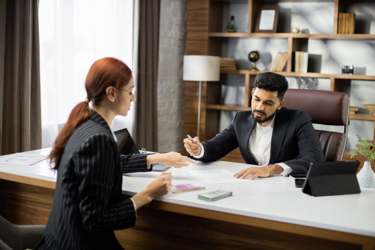 Confident businessman in black suit gives a salary to young red hair businesswoman.