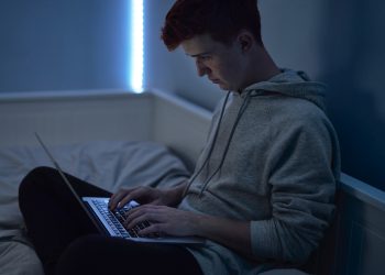 Focus caucasian teenage boy using laptop while sitting at night in his room
