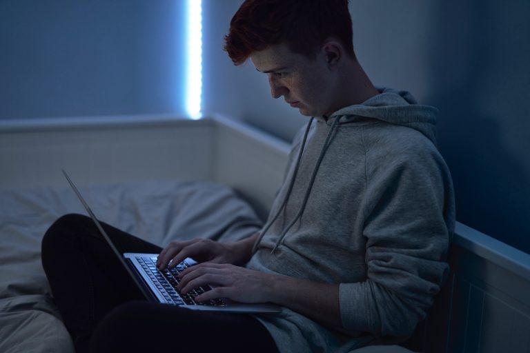 Focus caucasian teenage boy using laptop while sitting at night in his room