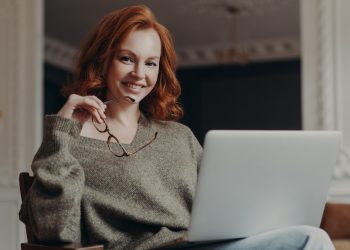 Professional positive redhead young European woman works on freelance, concentrated on remote job