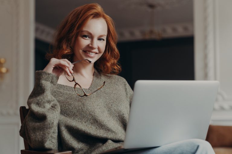 Professional positive redhead young European woman works on freelance, concentrated on remote job